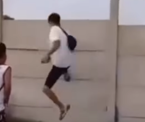 Meninos tentam derrubar muro com chutes, e um bloco se solta, atingindo a perna de um deles, próximo à canela, e causando um corte